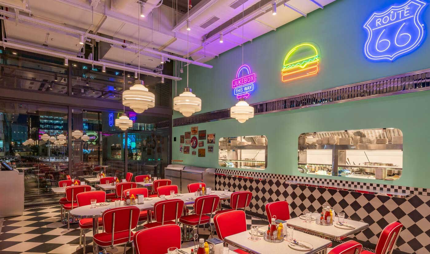 Neon Route 66, a burger sign, a "Jukebox This Way" arrow and a peek into the open kitchen.
